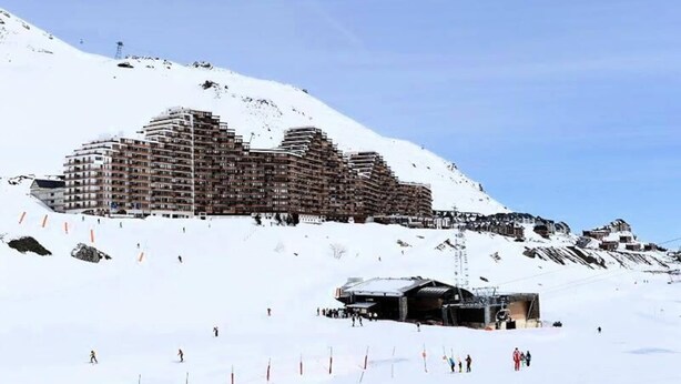Un hotel grande de varios pisos con un diseño arquitectónico moderno, ubicado en la ladera nevada de una montaña.