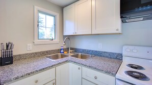 A kitchen with white cabinets, a double sink, a stove, and a window with a view of trees. - Lake-View Spofford Apartment w/ Shared Dock! (Spofford)