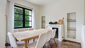 A dining area with a wooden table and six chairs, a fireplace, and shelves with glassware. - Douceur de vivre tropezienne: renovated house near beach and village (Gassin)