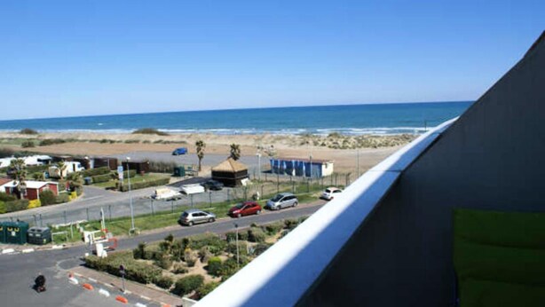 Vista costera con una carretera que lleva a una playa, un área de estacionamiento y un edificio con techo inclinado.