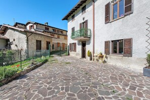 A courtyard with stone pavement, a building with a balcony, and a small table with chairs.