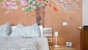Une chambre à coucher avec un lit, des coussins à motifs, une table de chevet avec une lampe et une fresque murale.