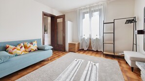 Une pièce avec un canapé bleu, un tapis blanc, un plancher en bois, un mur blanc, une porte et une fenêtre avec des rideaux.