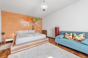 A bedroom with a bed, a sofa, a painting, and a chandelier.