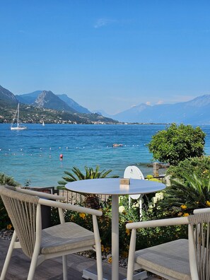 A table and two chairs facing a body of water with boats and mountains in the background.