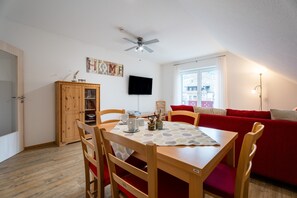 A dining area with a table, chairs, a ceiling fan, a TV, and a window with a view.