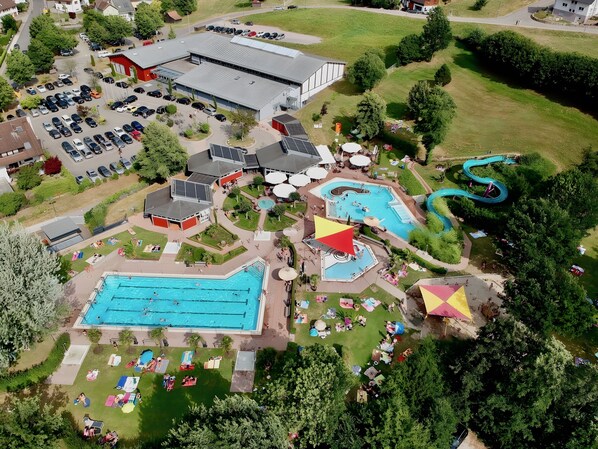 An aerial view of a resort with a large swimming pool, a water slide, and a parking area.
