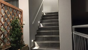 Una escalera con celosía de madera a la izquierda, barandilla de metal y felpudo negro en la parte inferior.