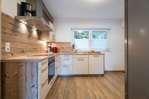 A modern kitchen with wooden cabinetry, a built-in oven, a stainless steel refrigerator, and a window providing natural light.