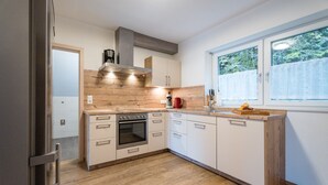 Una cocina moderna con armarios de madera, horno empotrado y ventana con vista a la vegetación.