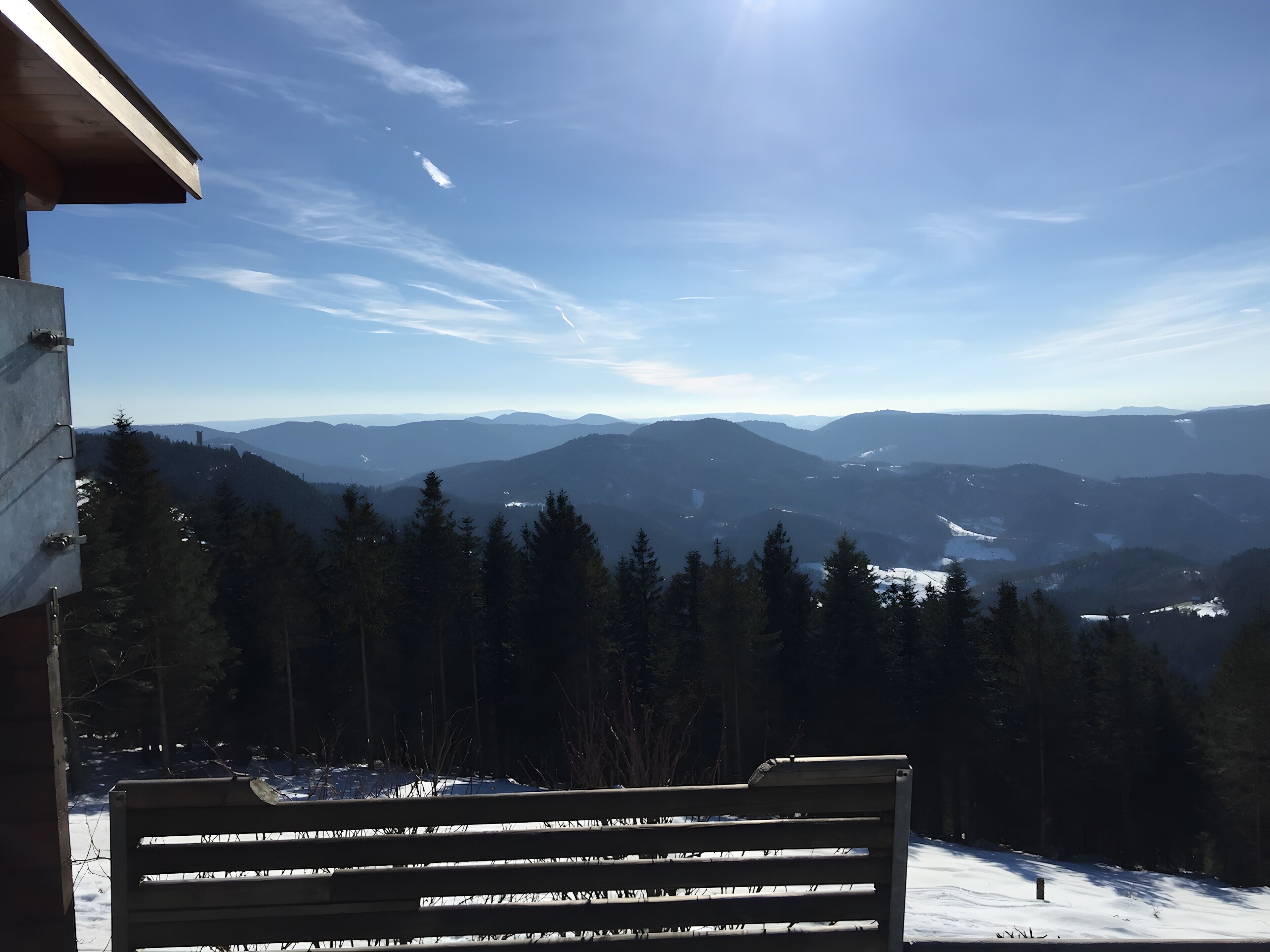 Eine Bank mit Blick auf eine verschneite Berglandschaft bei klarem Himmel.