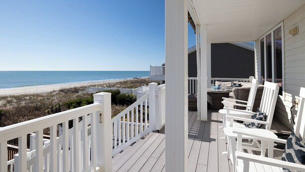 Une terrasse en bois avec des rampes blanches donnant sur une plage.