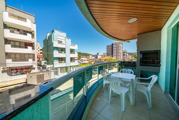 Een balkon met een houten plafond, een tafel en twee witte plastic stoelen.