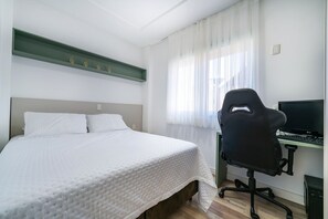 Een slaapkamer met een bed, een bureau met een computer en een stoel.