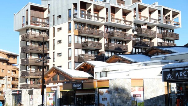 A multi-story hotel with balconies, a ski resort sign, and a shop named 'sherpa'. - Bright Apartment Close to the Slopes (Tignes)