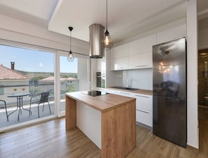 Una cocina moderna con una isla de madera, electrodomésticos de acero inoxidable y un amplio ventanal corredera que da a un patio exterior.