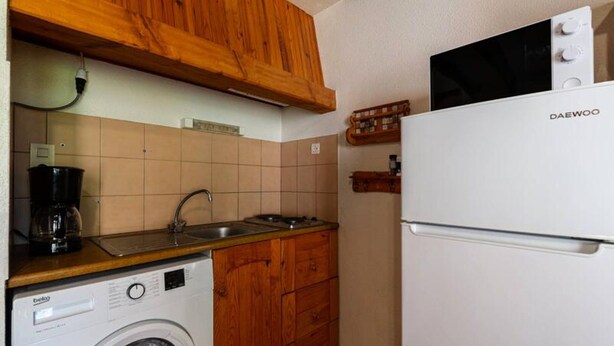 Une cuisine compacte avec des meubles en bois, un lave-linge, une machine à café et un réfrigérateur.