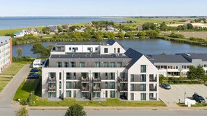 A modern multi-story building with balconies, a parking area, and a view of a lake. - Luxusappartement auf Nordstrand (Nordstrand)