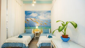 A room with two beds, a mural of a beach scene, a potted plant, and a small table. - Marina 48 Apartment on the Seafront with Sea Views, Wi-Fi and Air Conditioning (Port de Sóller)