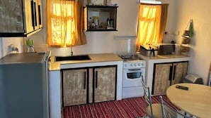 Une cuisine compacte équipée d’une cuisinière à gaz, d’un four et d’un évier. On y trouve également un four à micro-ondes posé sur le plan de travail, ainsi qu’une petite table avec des chaises.