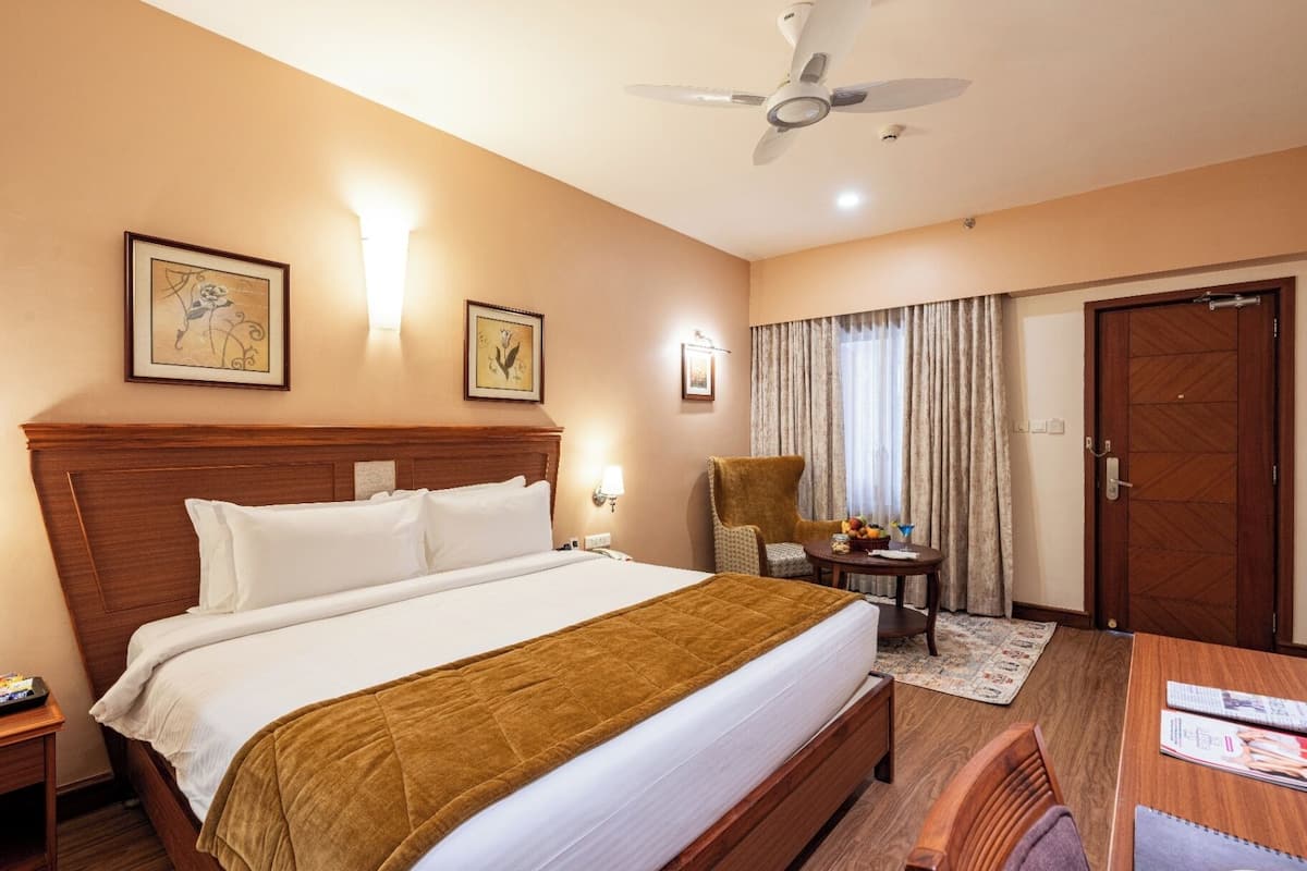 A hotel room with a large bed, a desk, a chair, a ceiling fan, and a door.