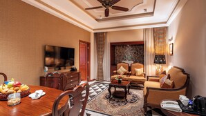 A hotel room with a dining area, a living room with a sofa set, a television, and a ceiling fan. - Jajati Courtyard (Korai)