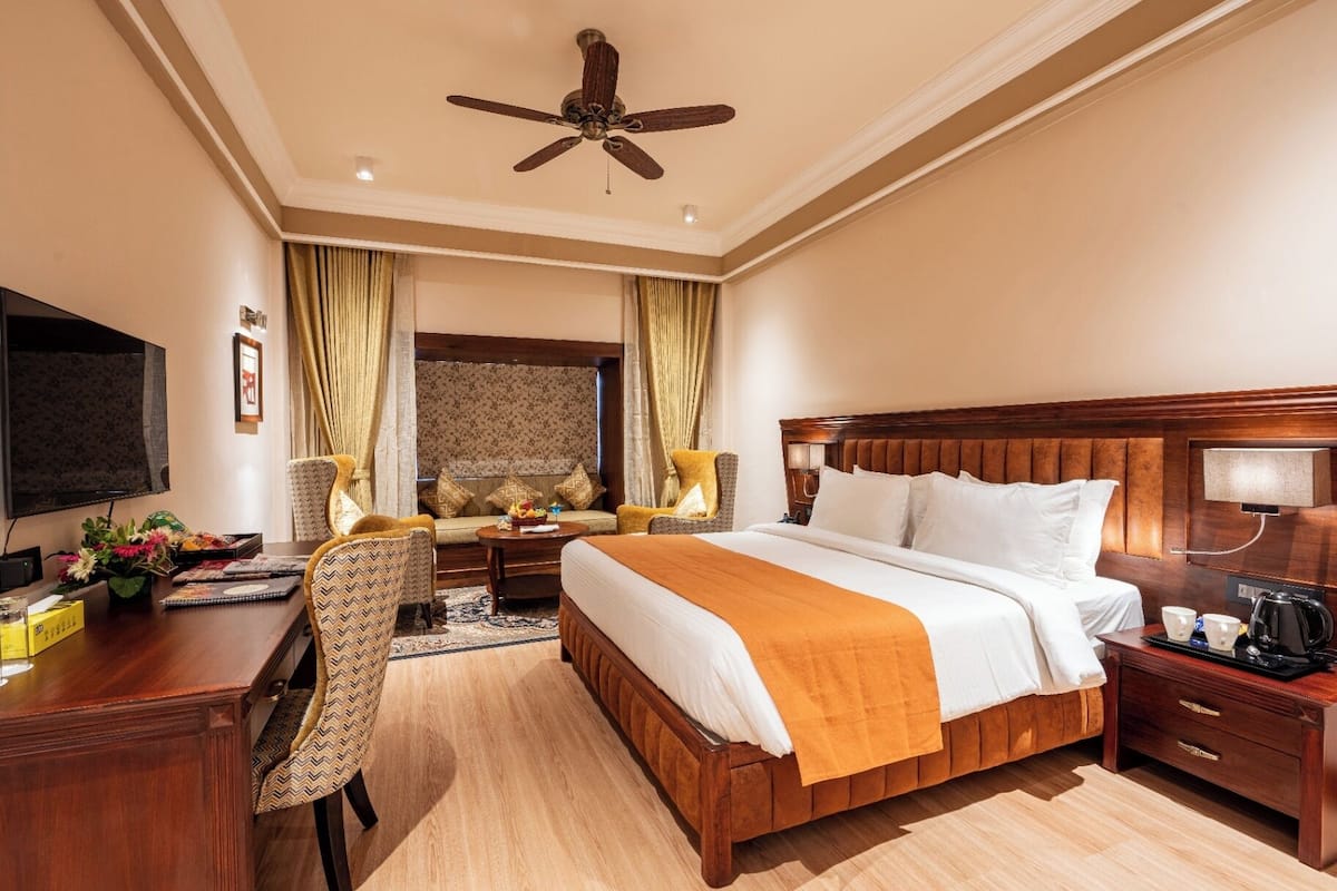 A hotel room with a large bed, a desk, a chair, a television, and a ceiling fan.