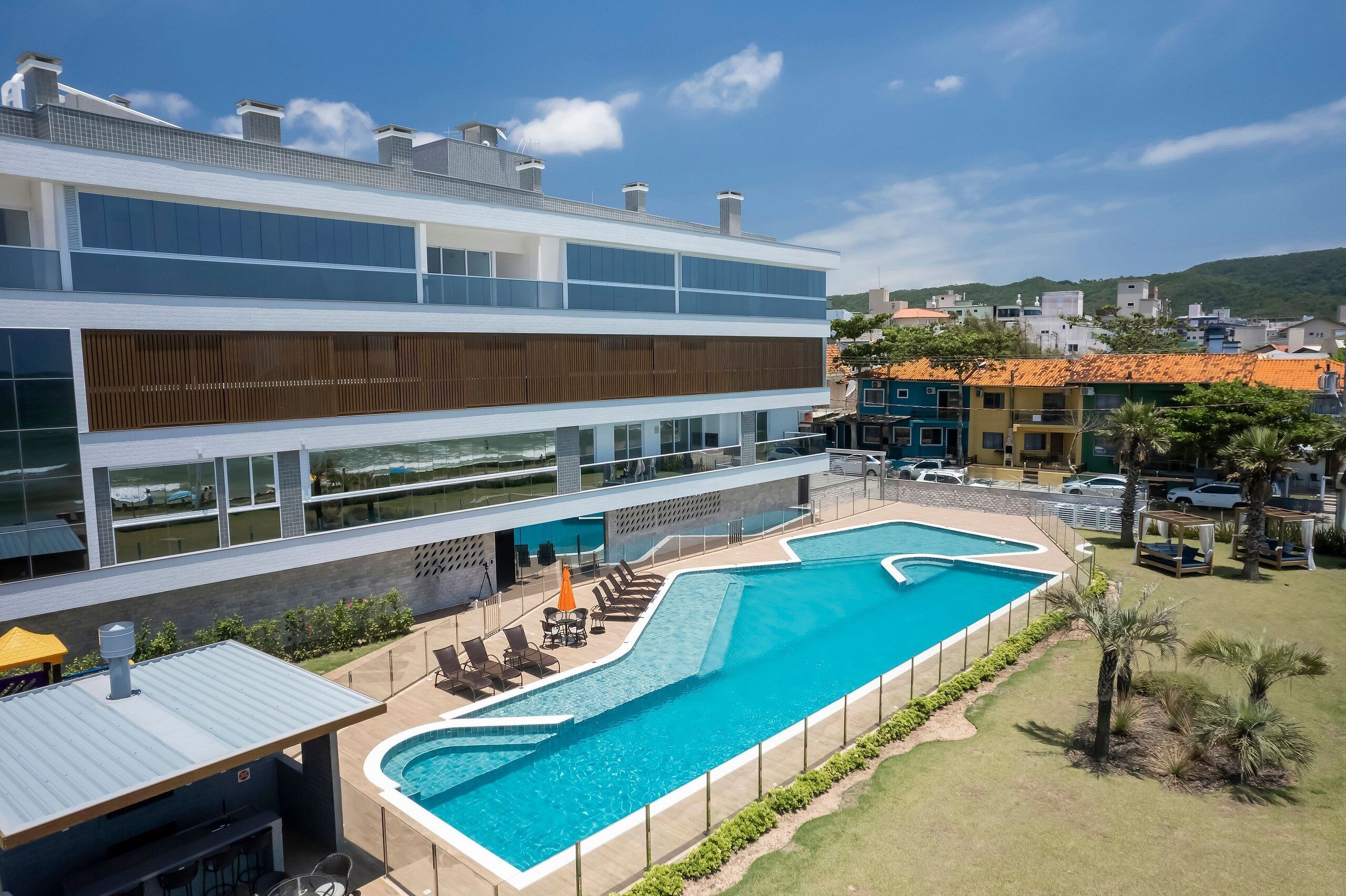 Un hotel moderno con una amplia piscina exterior, varios balcones y vistas del barrio circundante.