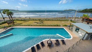A swimming pool with a view of the ocean, a deck with lounge chairs, and a modern building with large windows. - Duplex Alto Padrão Frente Mar c Piscina (Bombinhas)