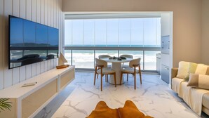 A modern living room with a large TV, a dining area with a table and chairs, and a sofa. - Duplex Alto Padrão Frente Mar c Piscina (Bombinhas)