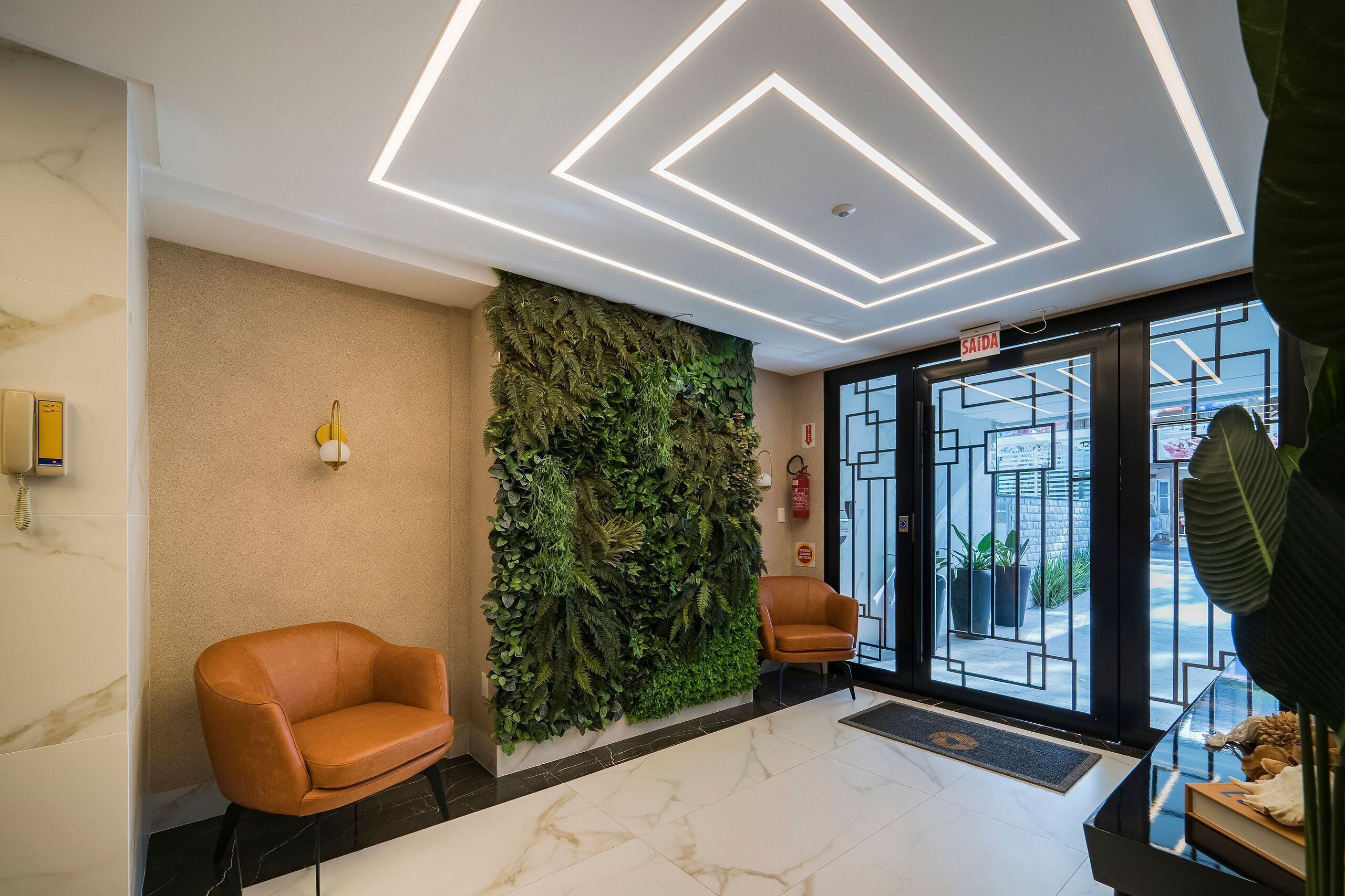 Eine moderne Lobby mit einer grünen Wand, zwei Ledersesseln, einem Marmorboden und einem geometrischen Deckenmuster.