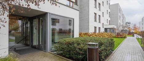 A modern building with a glass entrance, a paved walkway, and a well-maintained garden area.