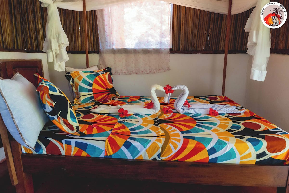 A bed with a colorful geometric-patterned bedspread, a white pillow, and a decorative swan made of fabric.
