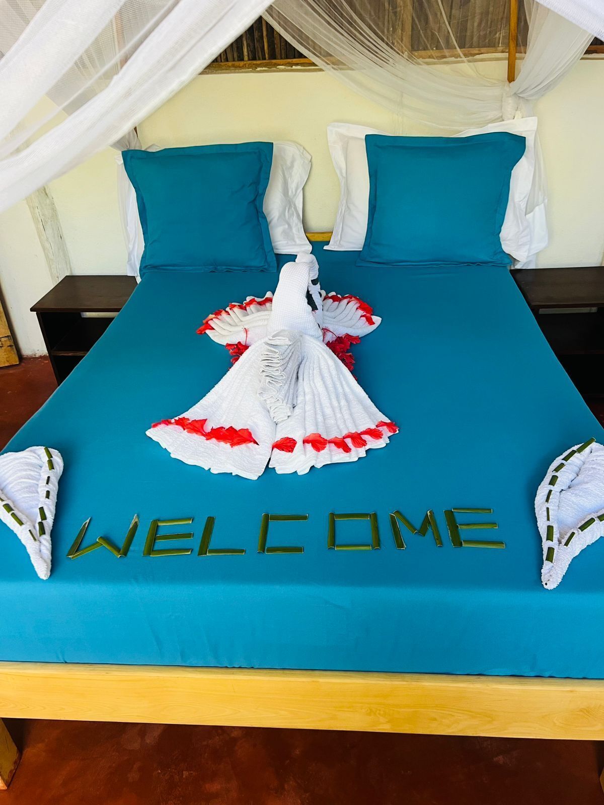 A bed with a blue bedspread, white pillows, and a decorative towel arrangement spelling "WELCOME".