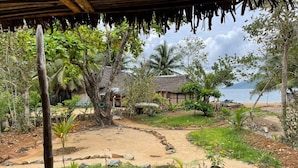 A tropical garden with a thatched-roof structure, a sandy path, and a view of the sea. - Djema Forest (Nosy Be)