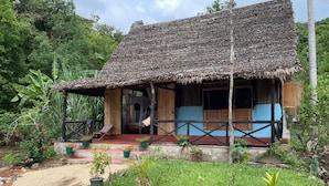 A rustic wooden house with a thatched roof, surrounded by lush greenery and a garden with potted plants. - Djema Forest (Nosy Be)