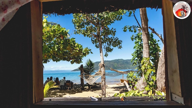 A beach view with a hammock and people sitting under a tree. - Djema Forest (Nosy Be)
