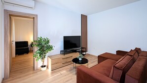 A modern living room with a flat-screen TV, a brown sofa, a wooden coffee table, and a potted plant. - Great 1-Bedroom Apartment in Trpanj - Pelješac (Trpanj)