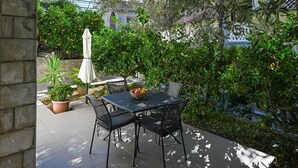 An outdoor patio with a table and chairs, surrounded by lush greenery and a stone wall. - Great 1-Bedroom Apartment in Trpanj - Pelješac (Trpanj)