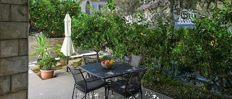 An outdoor patio with a table and chairs, surrounded by lush greenery and a stone wall.