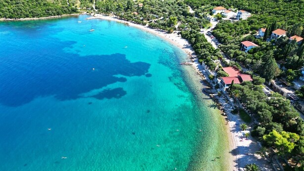 An aerial view of a coastal area with clear turquoise waters, a sandy beach, and a row of houses with red roofs. - Great 1-Bedroom Apartment in Trpanj - Pelješac (Trpanj)