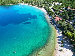 An aerial view of a coastal area with clear turquoise waters, a sandy beach, and a row of houses with red roofs. - Great 1-Bedroom Apartment in Trpanj - Pelješac (Trpanj)