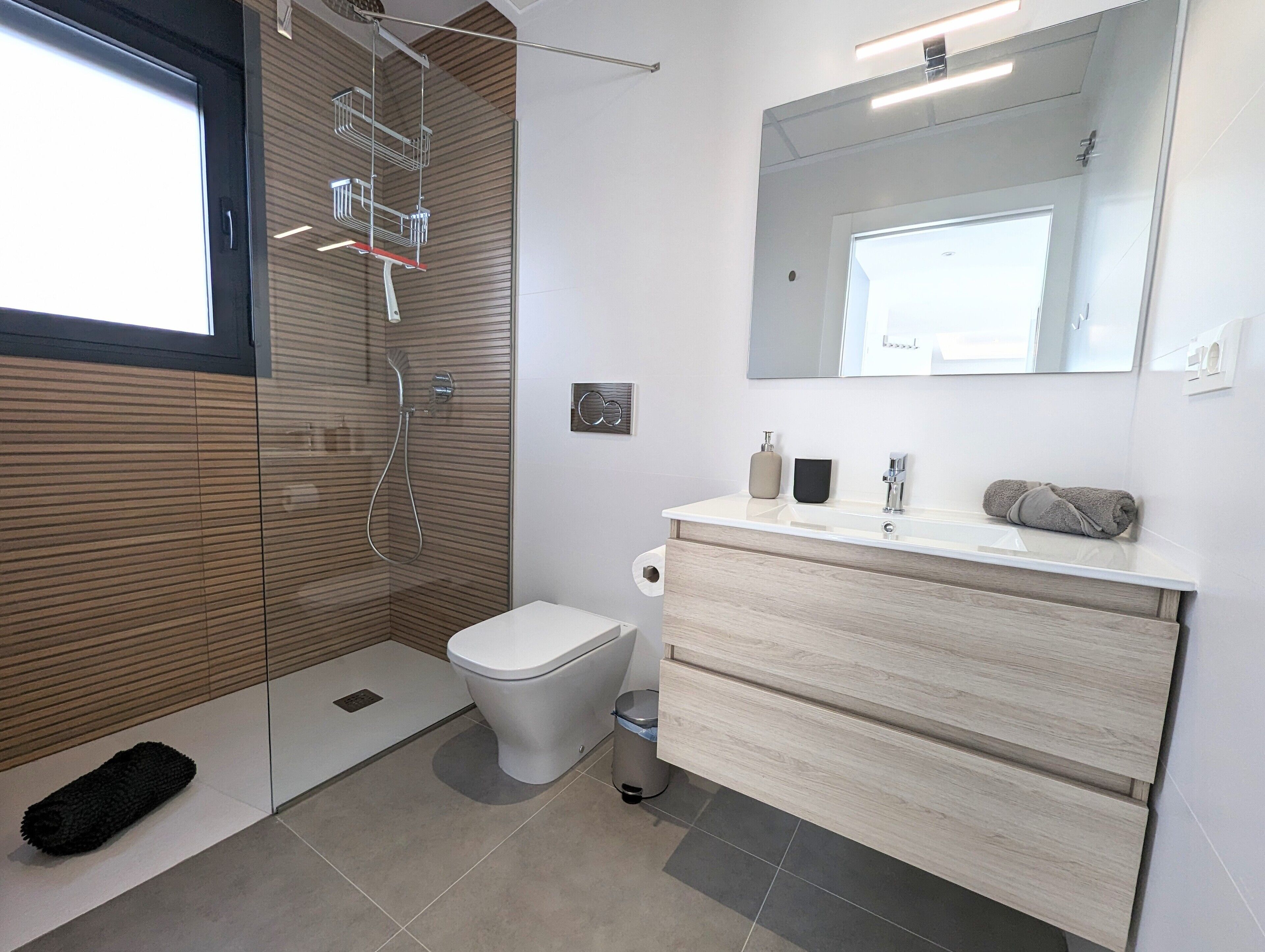 Un baño moderno con ducha, inodoro, tocador y un espejo grande.