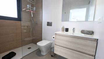 Un baño moderno con ducha, inodoro, tocador y un espejo grande.