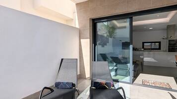 A modern outdoor seating area with two lounge chairs, a glass door leading to a pool, and a tiled floor.