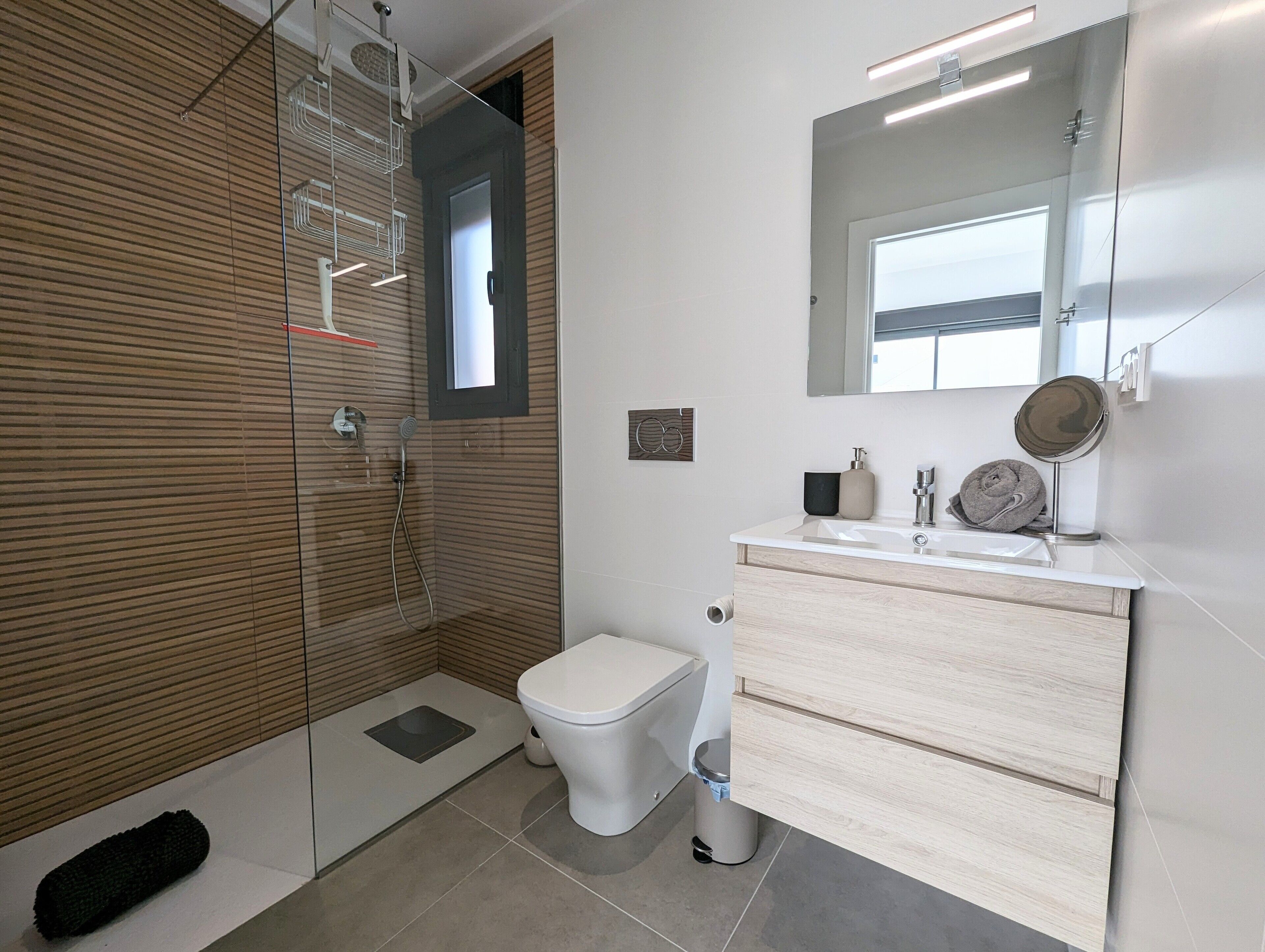 A modern bathroom with a glass shower enclosure, a toilet, a sink with a mirror, and a towel rack.