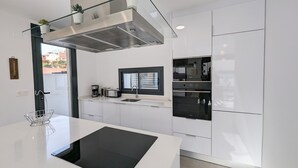 A modern kitchen with white cabinetry, a black induction cooktop, a built-in oven, and a stainless steel range hood. - Villa 'R-58 Luxury New Build' with Private Pool, Terrace and Wi-Fi (Los Montesinos)