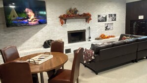 A living room with a fireplace, a TV mounted on the wall, a sofa, and a dining table with chairs. - Rustic Ranch Retreat, Farm stay, Firepit, Game Room, Stars (Pauls Valley)