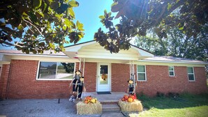 A brick house with a front porch, two hay bales with pumpkins, and a decorative figure. - Rustic Ranch Retreat, Farm stay, Firepit, Game Room, Stars (Pauls Valley)