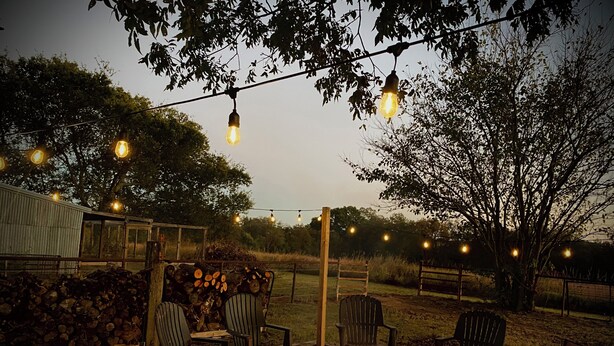 An outdoor seating area with chairs and a fire pit, surrounded by trees and string lights. - Rustic Ranch Retreat, Farm stay, Firepit, Game Room, Stars (Pauls Valley)